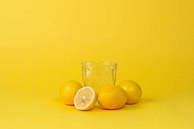 Lemons and empty glass cup on a yellow background