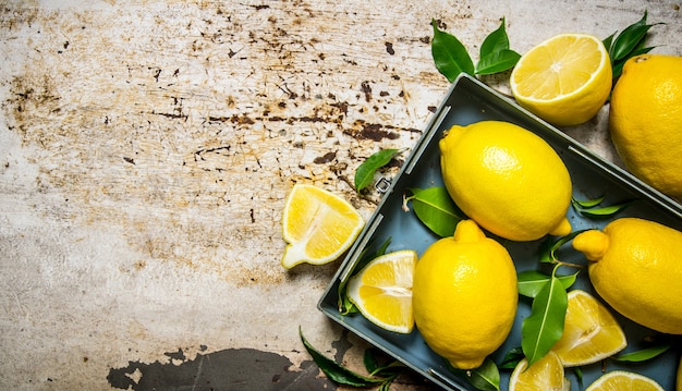 Lemons in a metal box with leaves. On rustic background. Free space for text . Top view