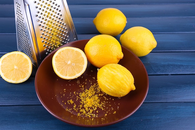 Лимоны на тарелке и терке на темно-синем деревянном фоне