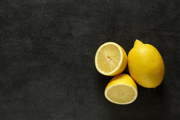 Lemons whole and cut three pieces on dark background top view space to copy text