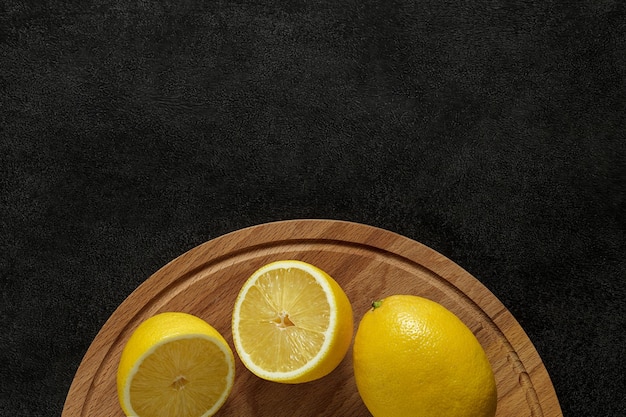 Photo lemons whole and cut on wooden chopping board on dark background top view space to copy text