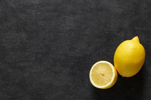 Lemons whole and sliced on dark background top view space to copy text