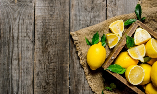 Lemons with leaves in a box on the fabric on wooden table. Top view