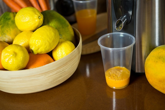 Photo lemons on wooden bowl with glass of juice at counter