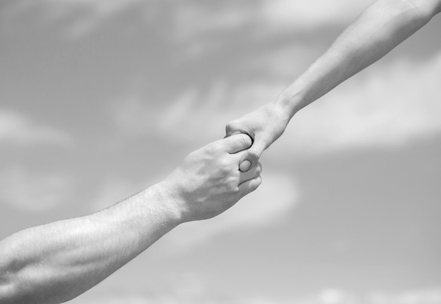 Lending a helping hand hands of man and woman reaching to each\
other support solidarity compassion and charity rescue giving a\
helping hand hands of man and woman on blue sky background