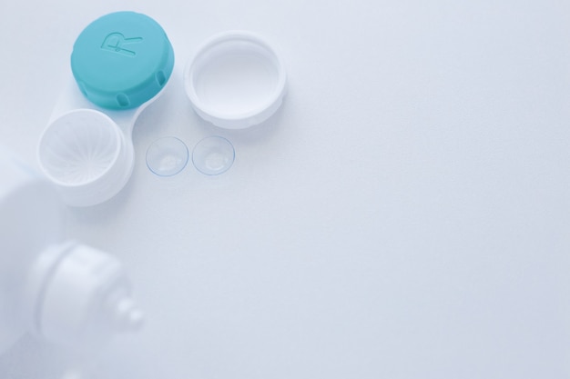 A lens container a lens storage liquid and two contact lenses lie on the side on a white background ...