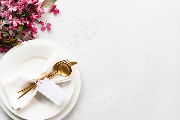 Lente elegantie tafel instelling met appelboom bloemen, gouden bestek en tag op witte tafel.