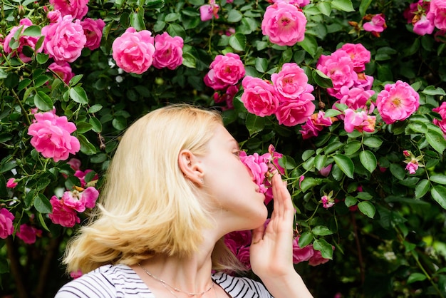 Lente en zomer Parfum en cosmetica Vrouw voor bloeiende rozenstruik Bloesem van wilde rozen Geheime tuinconcept Aroma van rozen Meisje schattig blond snuivende geur van roze bloei