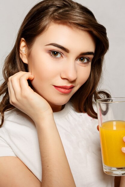 Lente, gezondheid, mensen, jeugd en schoonheid concept - met kop en schouders portret van aantrekkelijke Kaukasische lachende vrouw studio shot drinken sinaasappelsap gezichtshuid. Vrouw sap glas.