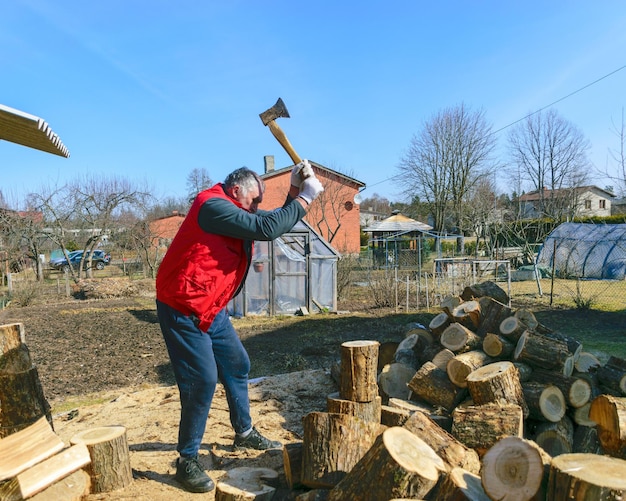 Foto lente landschap met een man in een rood vest een man in zijn tuin splijt brandhout klimaatverandering verwarmde energie energiecrisis