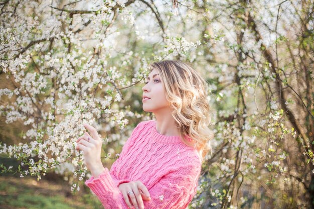 Lente portret van een jonge blonde in de buurt van een bloeiende boom. Gelukkige jonge vrouw. Voorjaar.