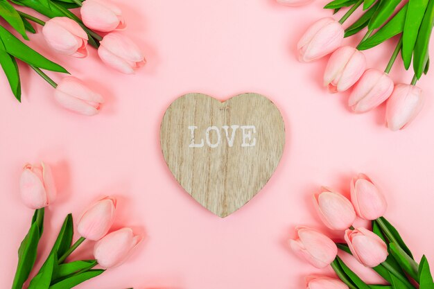 Lente roze tulpen en een houten valentijn in de vorm van een hart, op een roze achtergrond