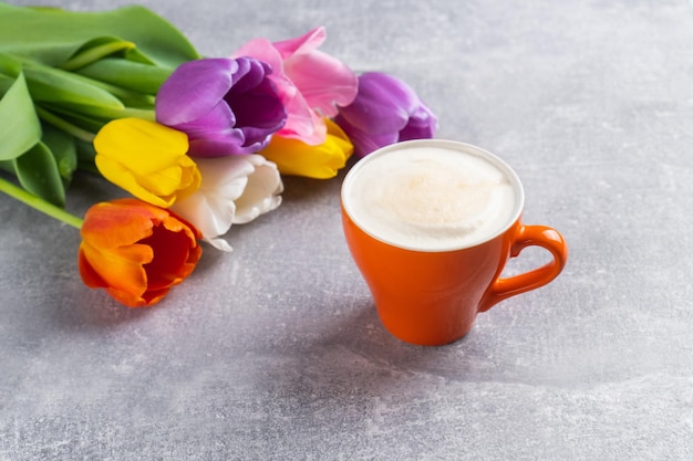 Lente veelkleurig tulpenboeket en kopje cappuccino op concrete achtergrond Bloemen en koffie