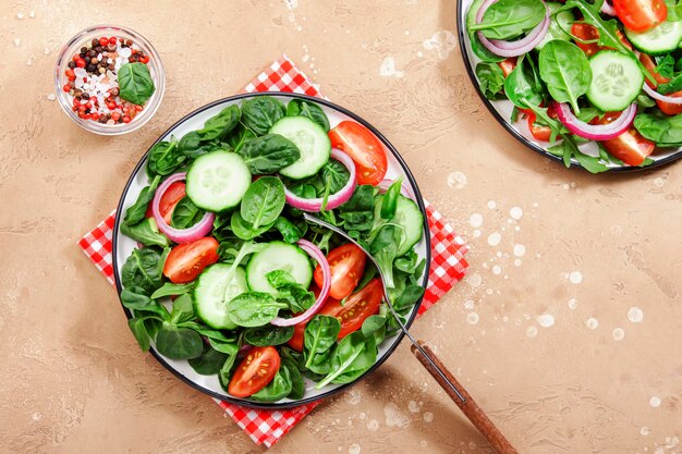 Lente veganistische salade met spinazie, cherrytomaatjes, veldsla en rode ui Gezonde voeding concept Beige stenen tafel achtergrond Bovenaanzicht