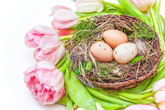 Lente wenskaart. Paaseieren in nest en het roze verse boeket van tulpbloemen op rustieke witte houten achtergrond