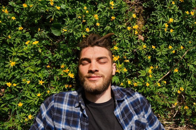 Lentebloemen close-up portret van de mens Sluit de ogen van de zon en plezier Jonge blanke hipster met dreadlocks en baard ligt op een open plek in het park tussen primula's van gele anemonen