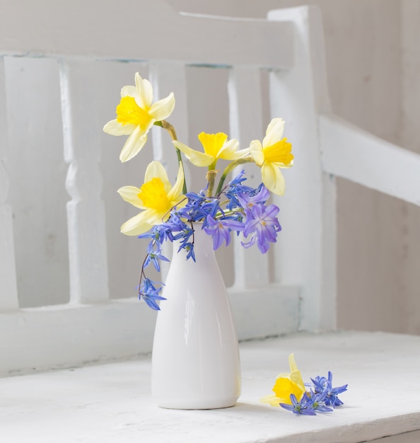 Lentebloemen in vaas op witte houten bankje