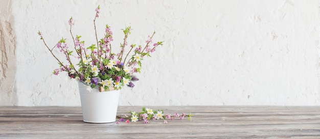 Foto lentebloemen in witte emmer op oude witte muur