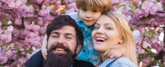 Foto lentebloesem banner met gelukkige familie. moeder vader en zoon. lente tijd. portret van gelukkige familie in bloeiende tuin.