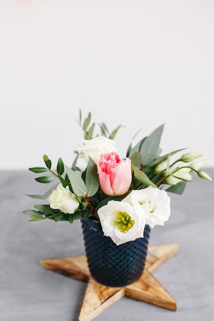 Lenteboeket in transparante glazen vaas op houten ster. Rozen, tulpen en lisianthus.