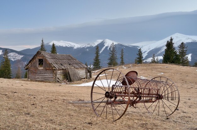 Lentelandschap met oude landbouwmachines en een houten schuur. uitzicht op de besneeuwde toppen van de bergen. karpaten, oekraïne, europa