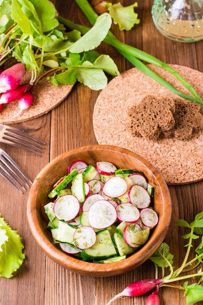 Lenten spring vegetable salad of cucumber, radish, greens and sunflower oil in a plate on a wooden table