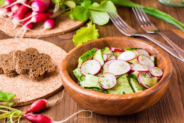 Lenten spring vegetable salad from cucumber, radish, greens and oil in a wooden plate