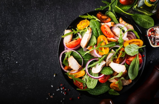 Lentesalade met spinazie gegrilde kip cherrytomaatjes rucola veldsla en rode ui Gezonde voeding concept Zwarte stenen tafel Bovenaanzicht Kopieer ruimte