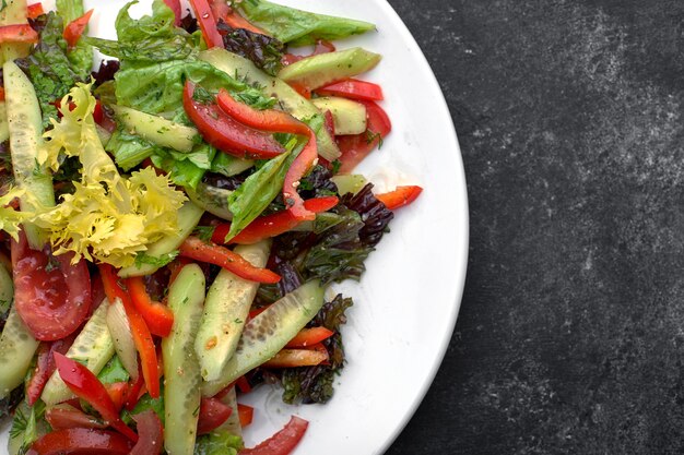 Lentesalade van verse groenten, komkommers, tomaten, sla, paprika op een witte plaat, op een donkere achtergrond