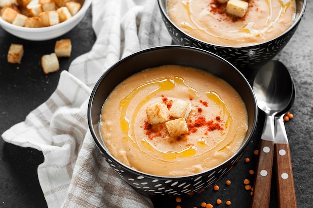 Lentil cream soup with paprika and crouton in black ceramic bowls on dark background