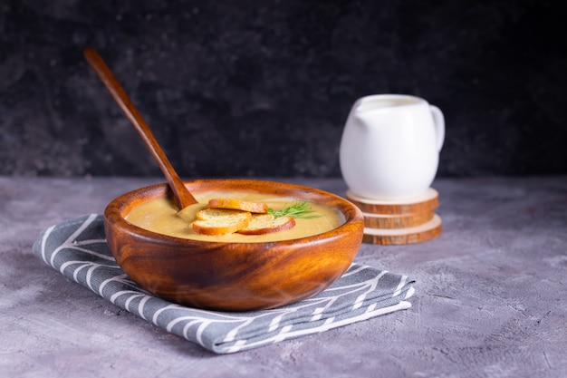 Lentil and pumpkin cream soup with dill in a wooden plate with a wooden spoon with creamer on wooden coasters on a gray surface