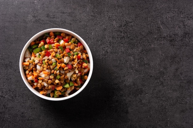 Lentil salad with peppersonion and carrot in a bowl on black slate background