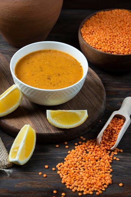 Photo lentil soup with fresh lemon and lentil clay pot composition on wood plate