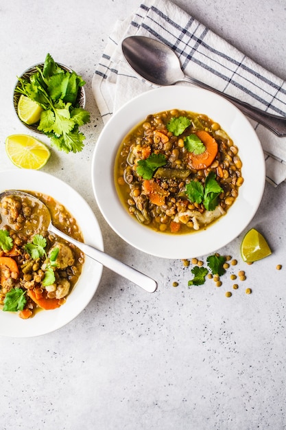 Lentil soup with vegetables in a white plate, white background, vertical. Plant based food, clean eating.