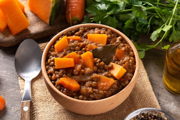 Ragù di stufato di lenticchie con zucca e carote in una ciotola sul tavolo di legno