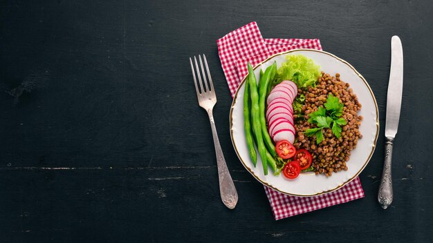 Lentil with radish cherry tomatoes beans and vegetables Healthy food On a black wooden table Top view Free space for text