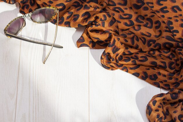 Leopard scarf, sunglasses on the white wooden background. 