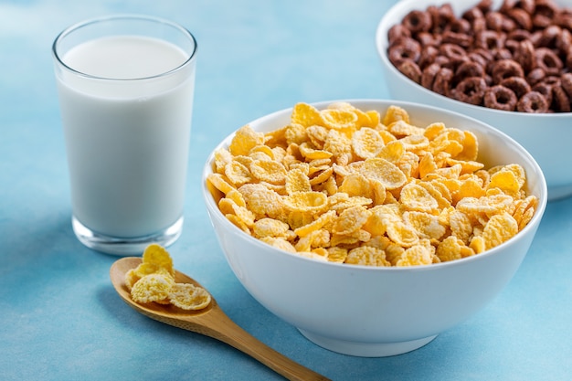 Lepel en kom met chocoladeringen, gele matte cornflakes en een glas melk voor droog ontbijtgranen