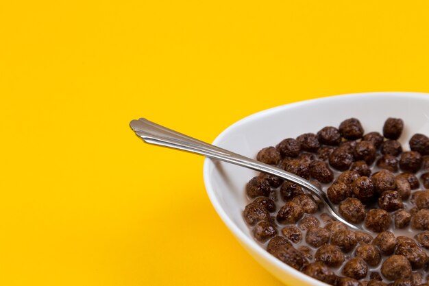 Lepel in witte kom met het graangewasballen van het chocoladekorrel en melk op geel