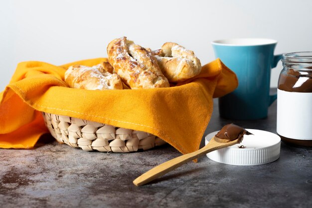 Lepel met chocolade naast mand met bladerdeeg koffiekopje en glazen pot gevuld met chocolade