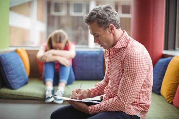 Leraar die op klembord met student op achtergrond in bibliotheek schrijft