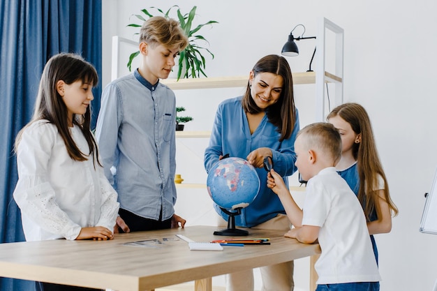 Leraar en kinderen in de klas kijken naar globe leraar helpt de les aan de kinderen in de klas aan een bureau uit te leggen