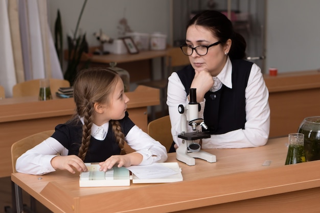 Leraar en leerling klein meisje zitten in school klaslokaal van biologie en werken met Microscoop