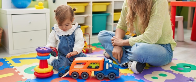 Leraar en peuter spelen met auto's speelgoed zittend op de vloer op de kleuterschool