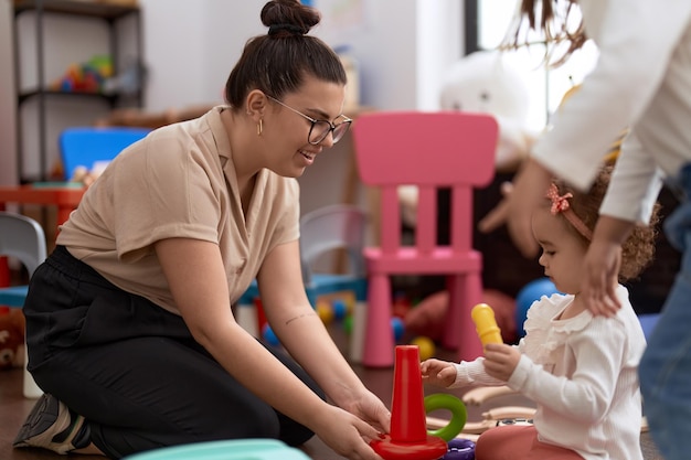 Leraar en peuter spelen met hoepels speelgoed zittend op de vloer op de kleuterschool