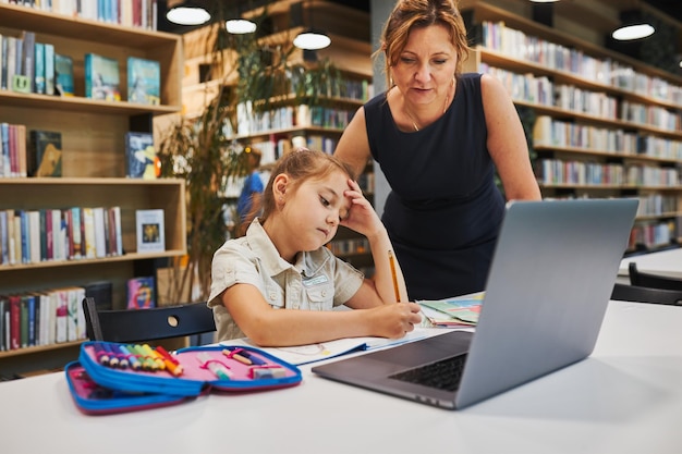 Leraar helpt met het oplossen en afmaken van een taak verveeld meisje doet haar huiswerk met behulp van een laptop