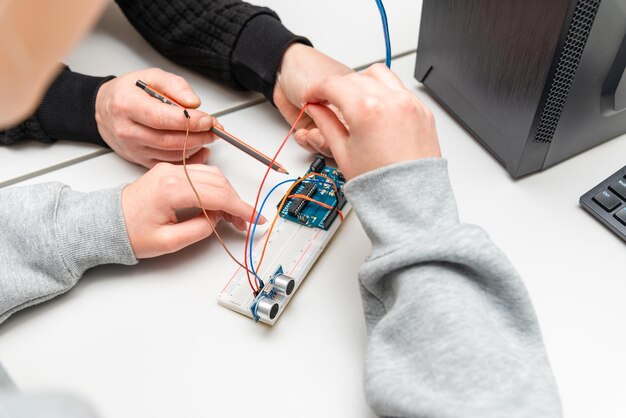 Leraar helpt zijn tienerstudent met een DIY-robot in de stengelopleidingslesStudent na de school computercodingklas bouwen en leren programmeren robotvoertuigArduino Ultrasone installatie