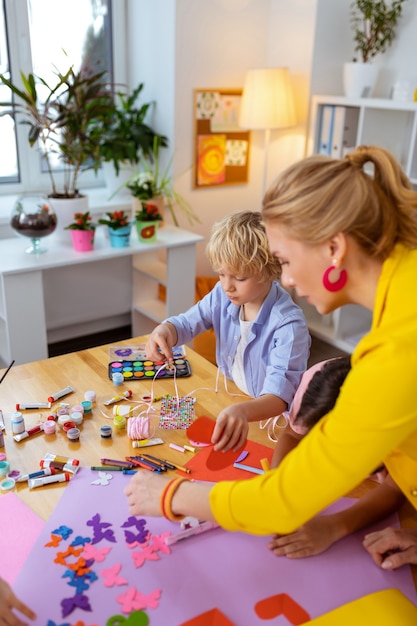 Leraar in de buurt van jongens. Blondharige basisschoolleraar die in de buurt van jongens staat terwijl ze knipsels maakt