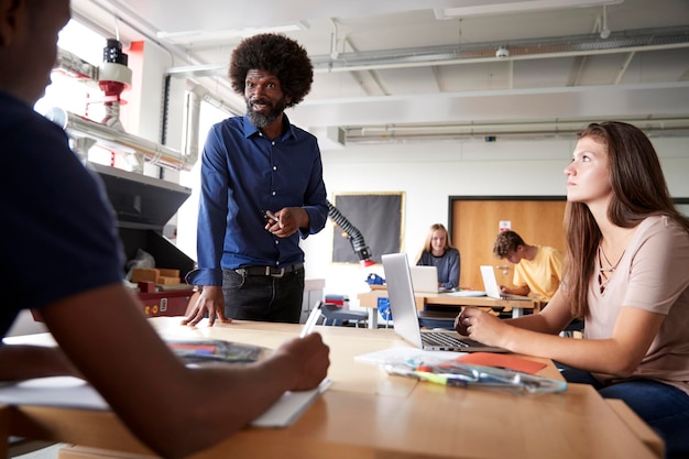 Leraar in gesprek met groep middelbare scholieren die op werkbanken zitten in ontwerp- en technologieles