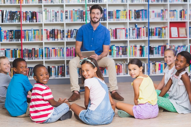 Leraar lesgeven kinderen op digitale tablet in bibliotheek